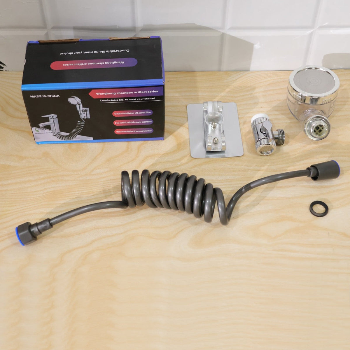 All components of the shower system, including the box, hose, spray head, and mounting bracket, are laid out on a wooden
