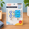 Two patterned adhesive hooks, one with blue dolphins and one with blue sailboats, displayed in packaging on a wooden surface.