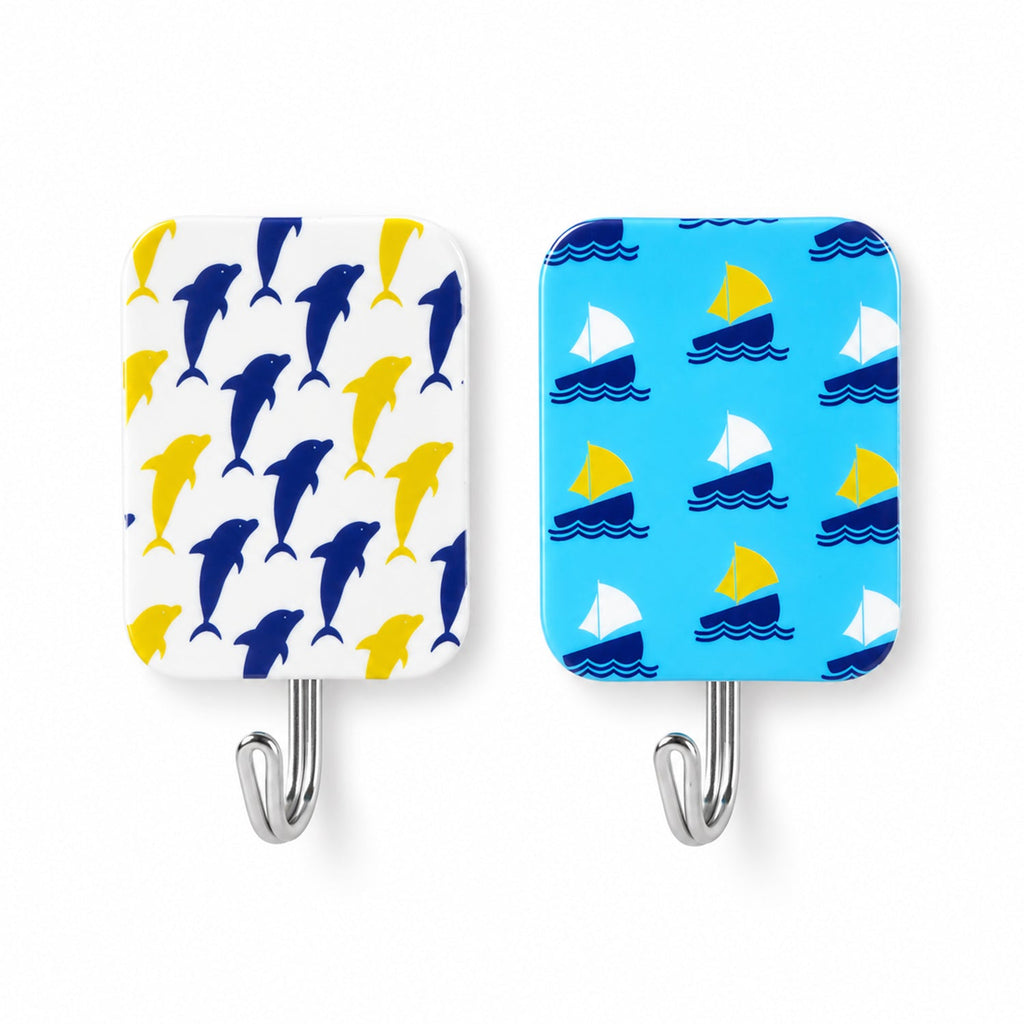 Close-up of two rectangular adhesive hooks, one with yellow and blue dolphins, the other with yellow and white sailboats.