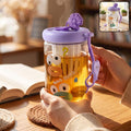 A person holds a clear glass tea sipper cup with a purple lid, infuser, and cartoon duck face design, filled with hot tea.
