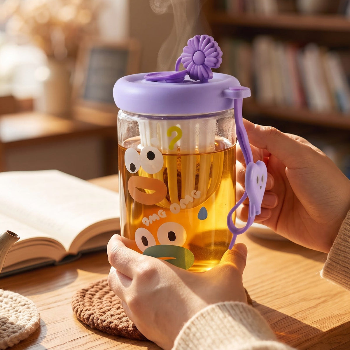 A glass tea sipper cup with a purple lid and cartoon duck face design, filled with hot tea, is held by a person over a
