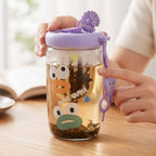 A person uses a glass tea sipper cup with a purple lid and cartoon duck face design, showing the infuser filled with loose