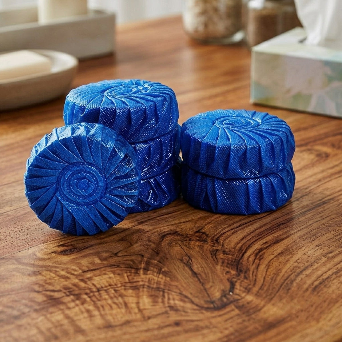 Several blue, round toilet cleaner tablets with a spiral pattern are stacked on a wooden surface.