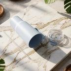 A light blue handled tumbler lies on its side on a marble surface with its clear lid and straw beside it.