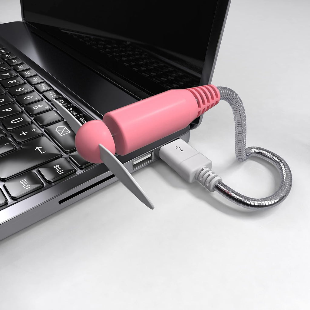 Pink USB mini fan with white blades plugged into the side of a black laptop on a white surface.