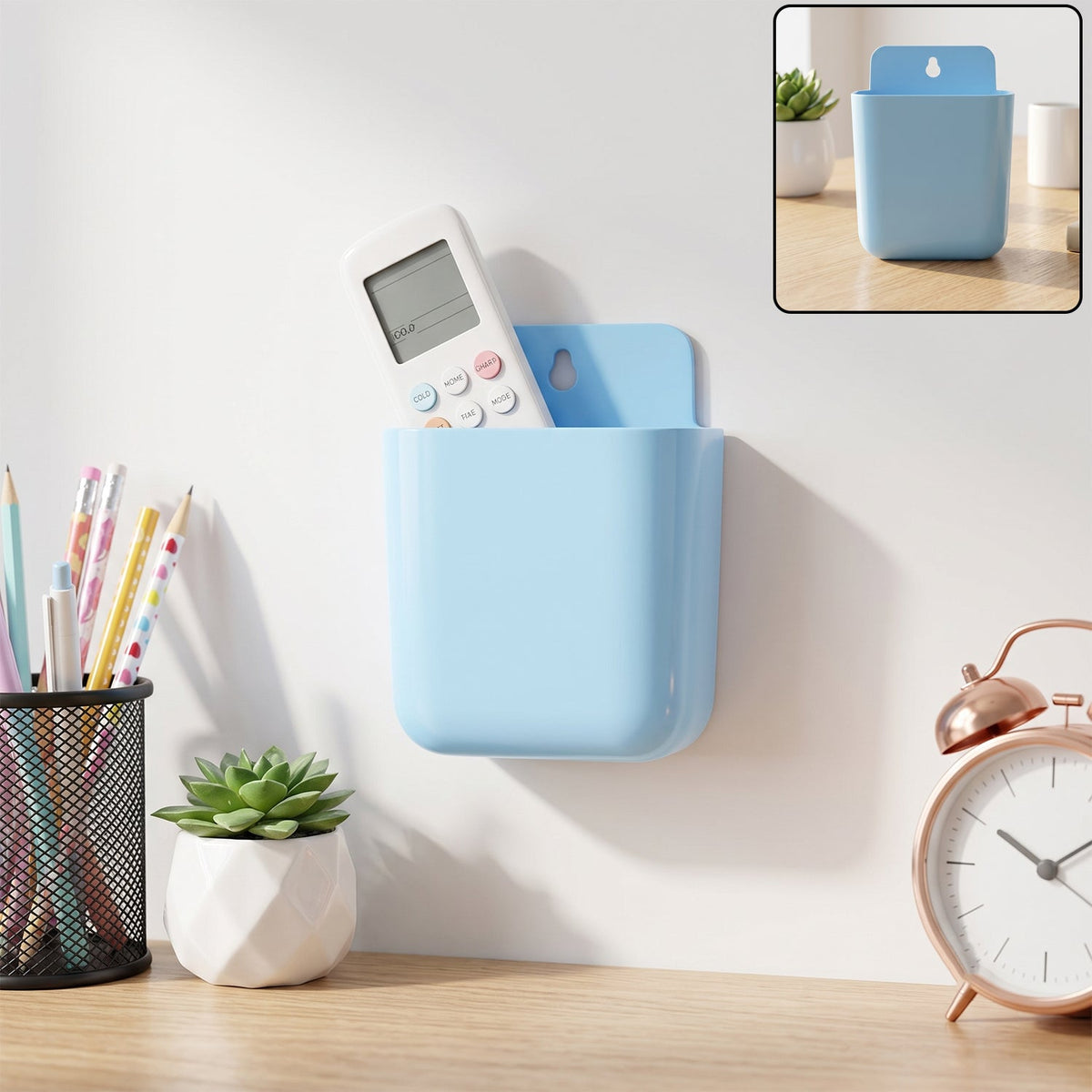 A light blue wall-mounted plastic storage pocket holds a white remote control above a desk with a plant and clock.