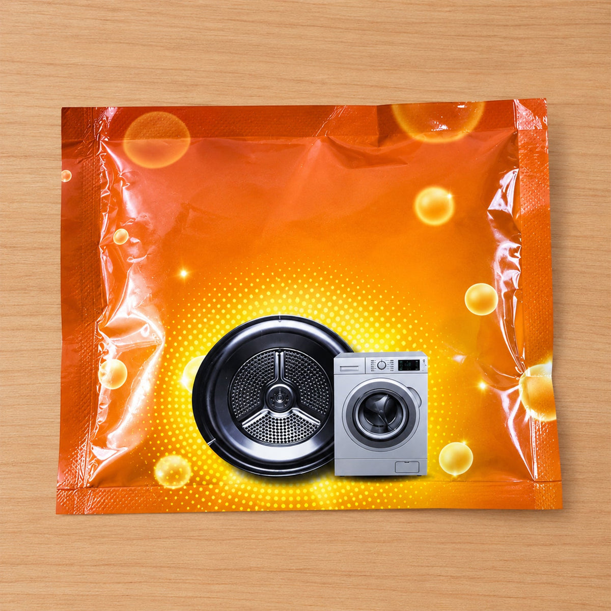 An orange powder sachet with a washing machine drum and miniature washing machine graphic on a wooden surface.