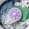A purple and white floating lint mesh bag in a washing machine with blue and green clothes.