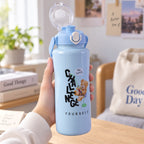 A hand holding a medium-sized light blue water bottle with an open flip-top lid in a bright room.