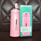 A pink vacuum flask with a silver lid and strap stands next to its retail box on a dark brown quilted surface.