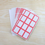 A stack of multiple sheets of red-bordered white writable labels fanned out on a light wooden surface.