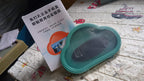 A teal cloud-shaped phone holder and its white instruction manual on a textured surface.