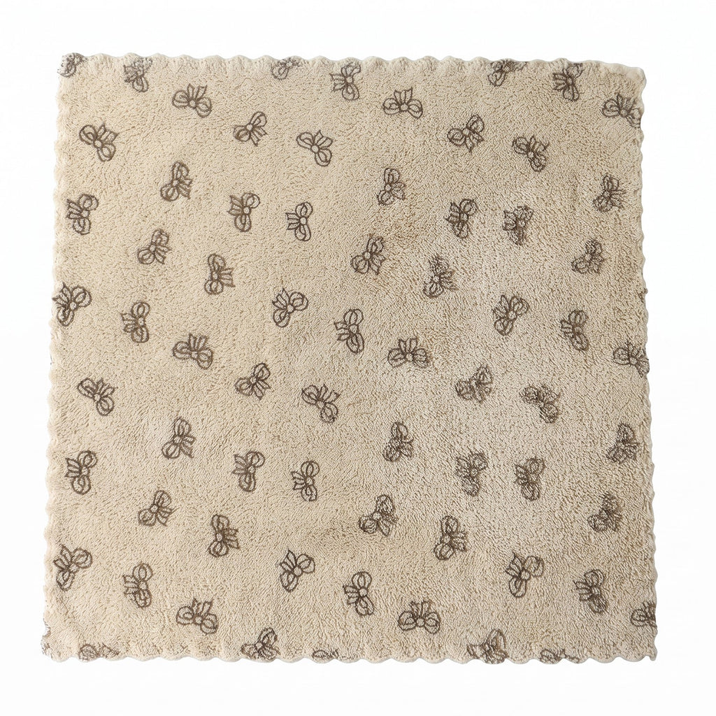 A beige microfiber towel with a dark bow pattern and scalloped edges lies flat on a white background.
