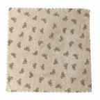 A beige microfiber towel with a dark bow pattern and scalloped edges lies flat on a white background.