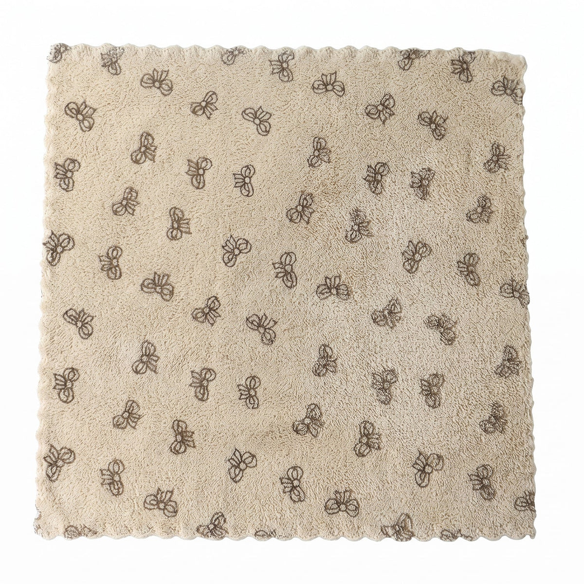 A beige microfiber towel with a dark bow pattern and scalloped edges lies flat on a white background.