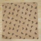 A beige microfiber towel with a dark bow pattern and scalloped edges lies flat on a light wood surface.