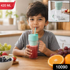 A young boy sips a red smoothie from a clear blender bottle with a mint green lid and straw in  kitchen setting.