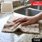 A hand wipes a wet granite countertop with a beige microfiber towel patterned with dark bows, next to a kitchen sink.