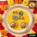A silver and yellow Radhe Radhe pooja thali set with two small decorative containers, surrounded by marigolds and rose,