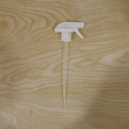 A white plastic spray nozzle with a long, clear tube is centered on a light wooden surface with visible grain.